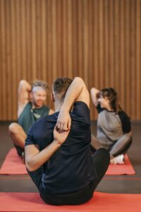 Adults in activewear practicing yoga and stretching indoors on mats.